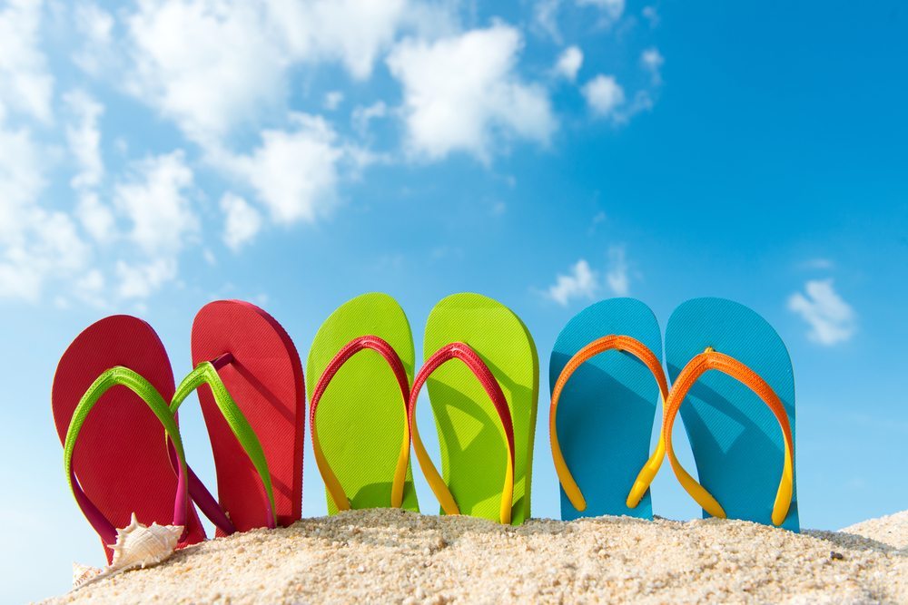6 flip flops thongs stuck in the sand against a blue sky background
