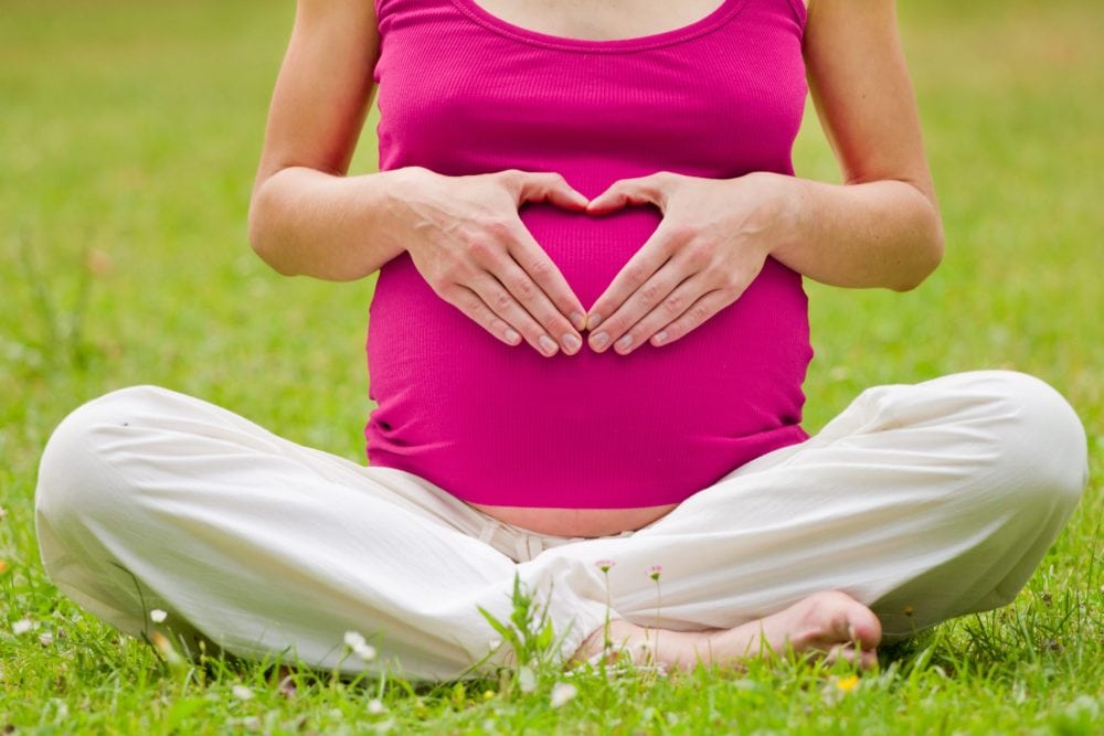 Pregnant woman in Pink sitting in a field of grass