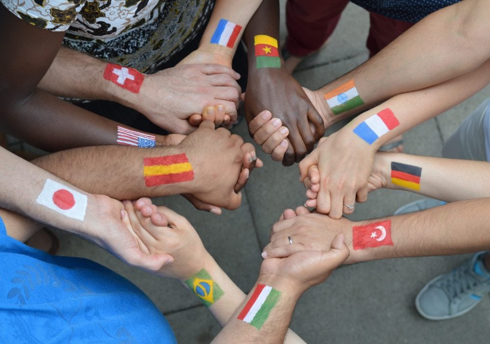 People of different ethnicities with country flags painted on them holding hands